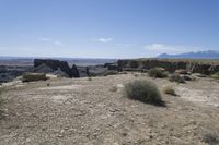 a view over a vast and barren landscape with rock formations in the distance and a small rock arch