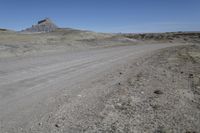 a dirt road is surrounded by some hills and desert like terrain as the vehicle sits on it