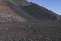 a cow that is standing in the dirt near a hill of mountain top material and rocks