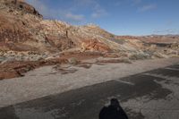 the person is standing on a dirt hill looking into the distance and shadow of a motorcycle