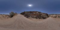 a large rock with dirt trail near it in desert area under full moon sky in daytime