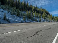 the empty highway is blocked off by the mountain on a nice winter day, with snow covered pine trees