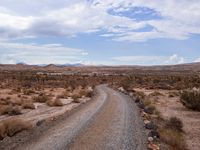 a gravel road in the desert with mountains in the background behind it, and scrub scrub scrub around