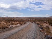 a gravel road in the desert with mountains in the background behind it, and scrub scrub scrub around