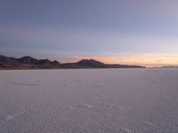 snow - covered flat landscape with a sunset in the distance at high desert area of desert mountains