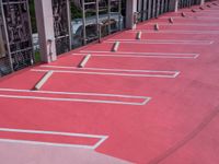 a sidewalk painted red with lines for parking lanes and vehicles parked in the background near fenced in area