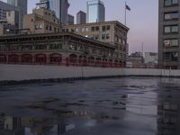 an empty parking lot with some buildings in the background and water on it and a flag pole overhanging the sidewalk