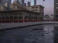 an empty parking lot with some buildings in the background and water on it and a flag pole overhanging the sidewalk