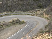 a lone road curves along a hilly hillside side, with shrubs and bushes surrounding it