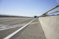 a skateboard on the edge of an asphalt road next to a rail way with mountains in the distance