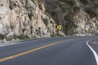 two yellow signs on the corner of a curve road in the mountains as if they were trying to cross one