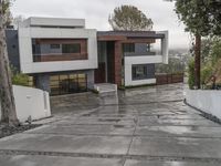 a very modern residence designed for entertaining on a rainy day in california city with large glass front doors and trees outside