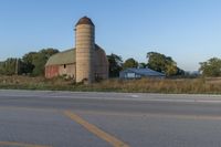 the view of a farm with tall silos on the other side of a country road