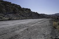 dirt road in the mountains surrounded by rock formations and shrubs, on a bright sunny day