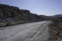 dirt road in the mountains surrounded by rock formations and shrubs, on a bright sunny day