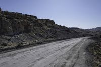 dirt road in the mountains surrounded by rock formations and shrubs, on a bright sunny day