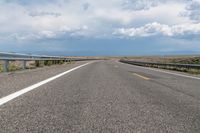 a view of the road with the mountains in the distance on the horizon, while some clouds gather