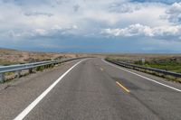 a view of the road with the mountains in the distance on the horizon, while some clouds gather