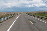 a view of the road with the mountains in the distance on the horizon, while some clouds gather