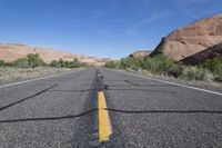 the empty road that is running through the desert land and mountains in the background with the shadows on the pavement