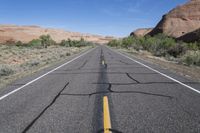 the empty road that is running through the desert land and mountains in the background with the shadows on the pavement