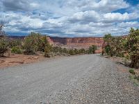 a motorcycle is on a gravel road through the desert below trees and mountains with red rocks on both sides of a rocky road