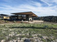 a house with a wooden roof stands on some grassy land next to a fence and mountain range