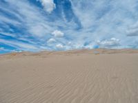 a sand hill with small vegetation in it under a cloudy sky filled with clouds and blue skies