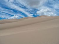 some very tall and wide dunes in the sky with clouds above it and a person walking away