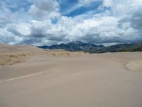 a sandy area with mountains in the distance under clouds with some footprints in the sand