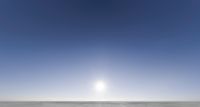 an empty field with dirt on it and a bright blue sky in the background that has sunlight coming through the middle