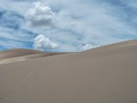 man walking alone through the desert under a blue cloudy sky, with a backpack in front of him