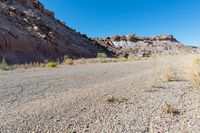 a barren road near the edge of a large mountain range with desert grass in the foreground, surrounded by small bushes