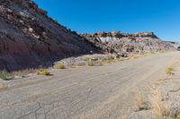 a barren road near the edge of a large mountain range with desert grass in the foreground, surrounded by small bushes