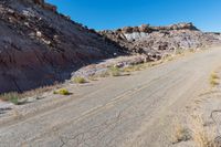 a barren road near the edge of a large mountain range with desert grass in the foreground, surrounded by small bushes