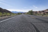 a lone road in the desert with mountains in the distance and trees in the foreground