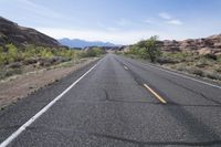 a lone road in the desert with mountains in the distance and trees in the foreground