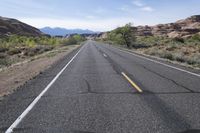 a lone road in the desert with mountains in the distance and trees in the foreground