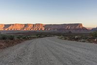 a wide open gravel road with mountains in the background at sunset near monument state park