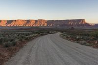 a wide open gravel road with mountains in the background at sunset near monument state park