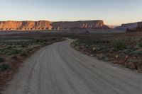 a wide open gravel road with mountains in the background at sunset near monument state park