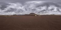 a landscape of sand and hills, with animals grazing in the foreground and a storm clouds over the top