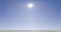 a young man skates on an open, barren surface of snow covered ground as the sun shines over it