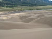 some people are riding horses in the sand dunes near the mountains and a river or stream