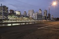 an empty street is at a busy road with tall buildings on both sides of the river and cars parked in the distance