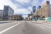 an empty street with buildings in the background and some cars driving down the road with no people