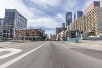 an empty street with buildings in the background and some cars driving down the road with no people