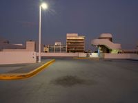 a empty parking lot near a building in the distance at night with street lights shining above the buildings