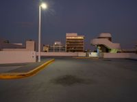 a empty parking lot near a building in the distance at night with street lights shining above the buildings