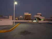 a empty parking lot near a building in the distance at night with street lights shining above the buildings